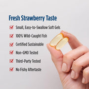 A hand holding two soft gel capsules against a light gray background, next to a text list describing the product as fresh strawberry taste with bullet points about size, wild-caught fish, sustainability, and testing.